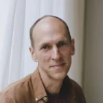 The Rest of Our Lives The Rest of Our Lives author Ben Markovits in brown shirt by white-curtained window