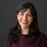 The World at Home author Ginny Kubitz Moyer color portrait with long dark hair, smiling.