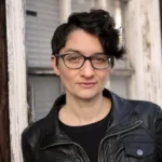 Hemlock Hemlock author Melissa Faliveno wearing a black leather jacket, glasses, short wavy hair at a window.