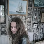 The Tide Child Trilogy author RJ Barker photographed against an art-filled wall with a ship painting.