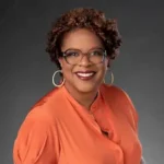 Kin author Tayari Jones in orange blouse, smiling, glasses and hoop earrings.