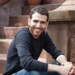 The Optimists The Optimists author Brian Platzer smiling, sitting on outdoor stairs.