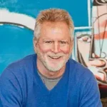 Deadly Gold Rush author Landis Wade in blue sweater, colorful background.