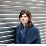 Beginning Middle End author Valeria Luiselli standing against a metal corrugated background.