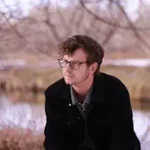 Out of Body Out of Body author Chris Vanjonack sitting by a serene lake.
